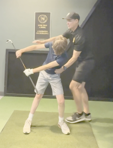 Black Polo Golf instructor guiding a youth golfer through swing positions